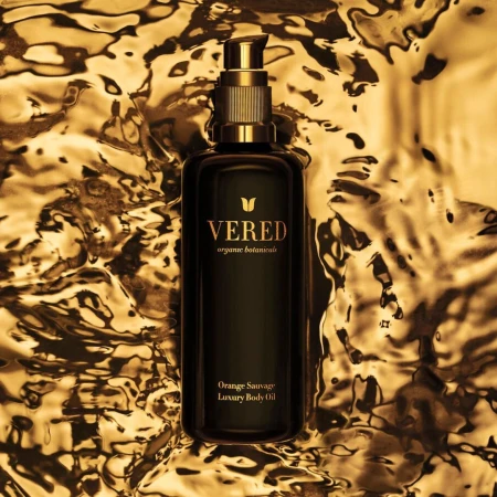 Elegant black VERED Organic Botanicals bottle with gold accents, featuring luxury body oil, set against a textured gold background.