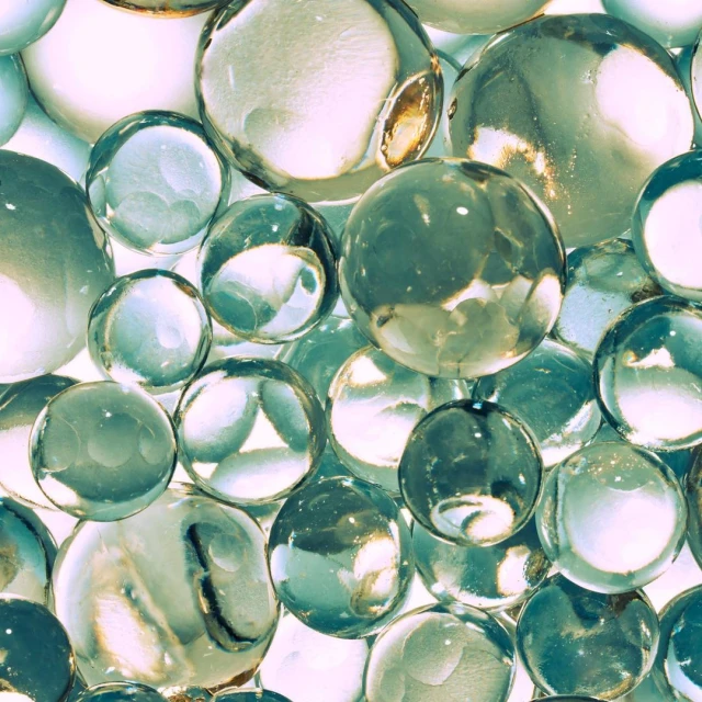 Close-up studio shot of transparent decorative spheres filling the frame with soft pink and green hues, creating a textured pattern.
