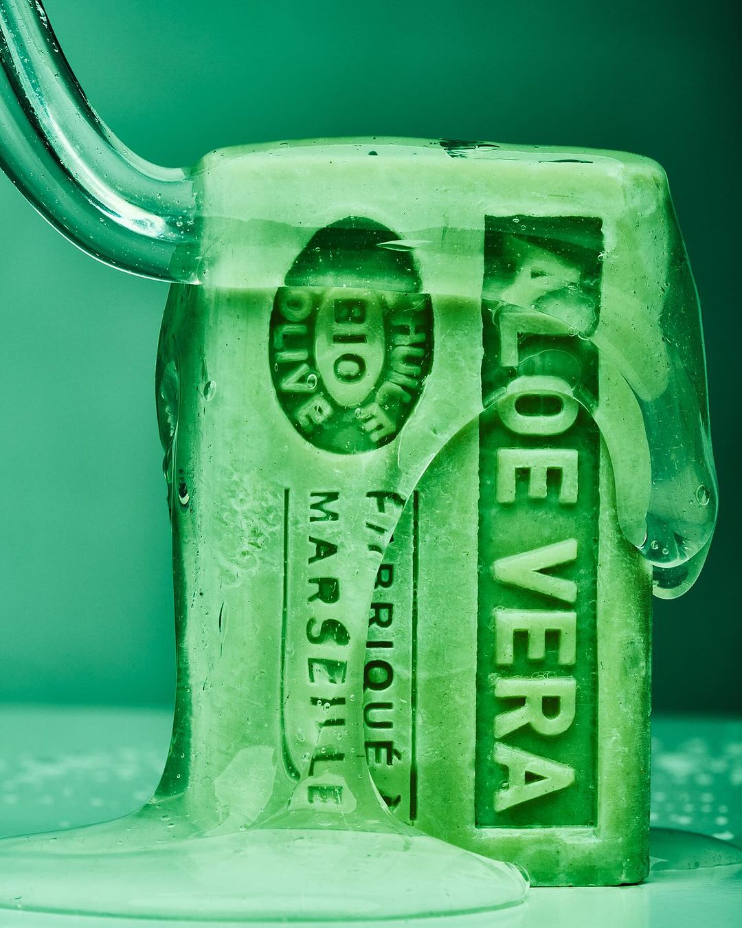 Close-up studio shot of a green bar of Aloe Vera soap under running water, highlighting its natural, moisturizing properties and fresh scent.