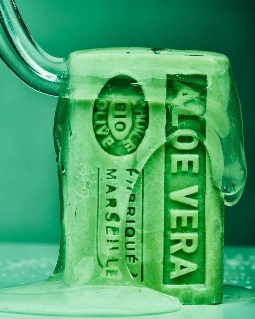 Close-up studio shot of a green bar of Aloe Vera soap under running water, highlighting its natural, moisturizing properties and fresh scent.