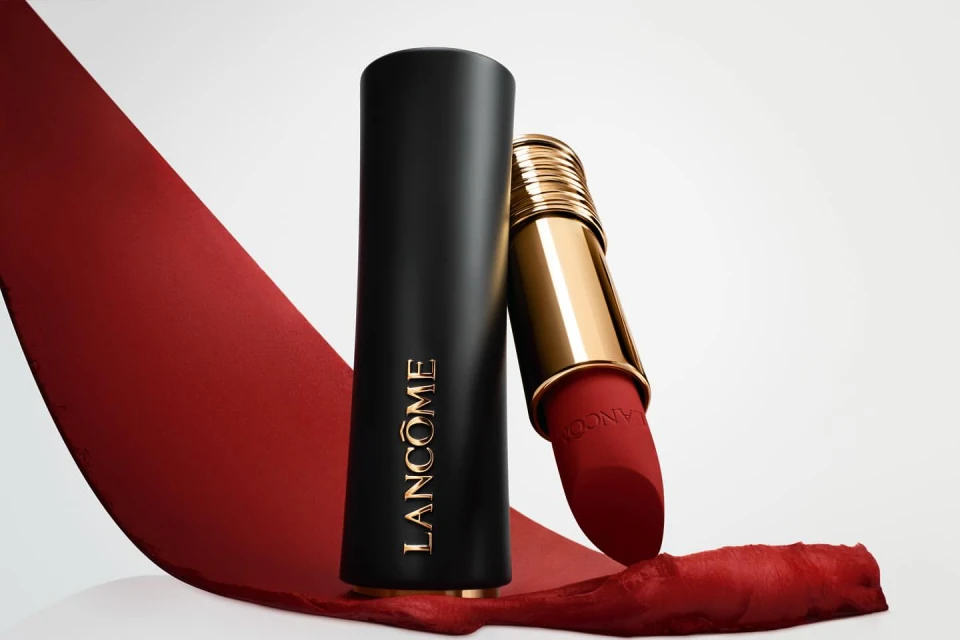 Still-life of red Lancôme lipstick with gold accents on a white surface with a red ribbon, product shot, beauty and makeup.