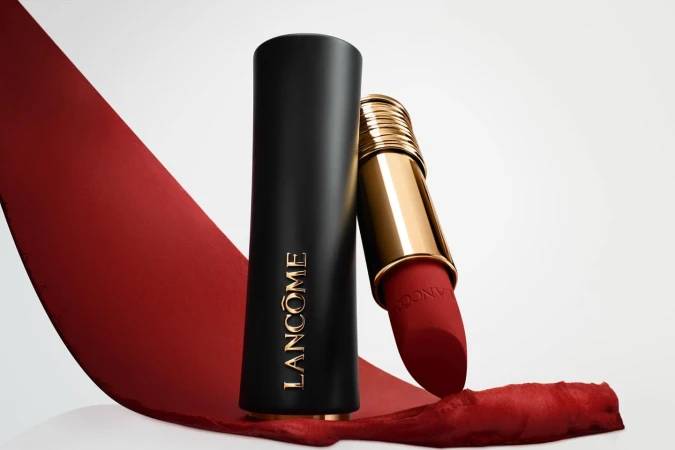 Still-life of red Lancôme lipstick with gold accents on a white surface with a red ribbon, product shot, beauty and makeup.