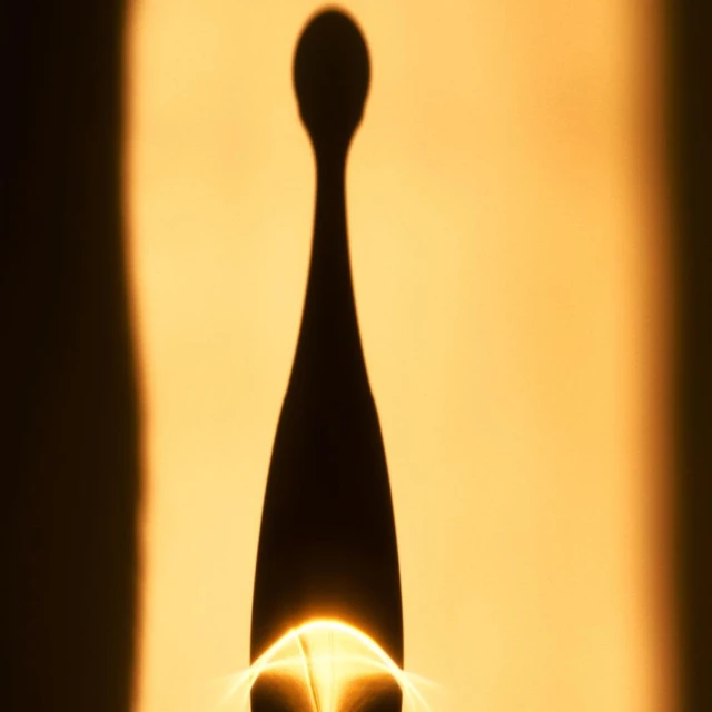 Abstract image featuring the shadow of a perfume bottle with a round top and a long neck against a light orange background.