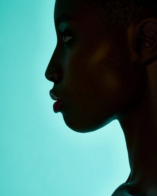 Profile of a dark-skinned young adult woman with red lipstick against a cyan background, showcasing studio lighting and beauty.