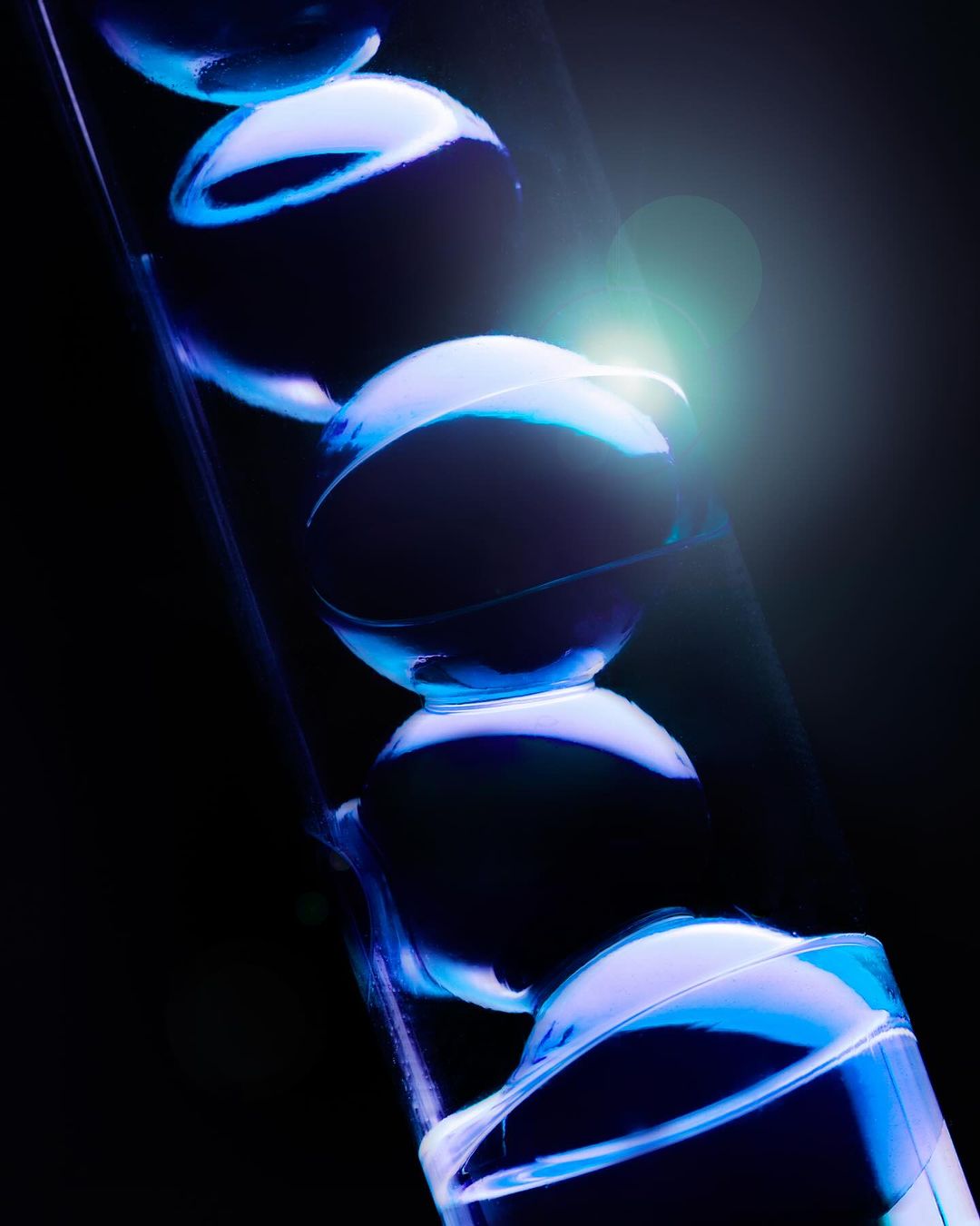 Abstract macro shot of illuminated transparent spheres stacked in a clear tube, creating a mesmerizing visual effect against a dark background.
