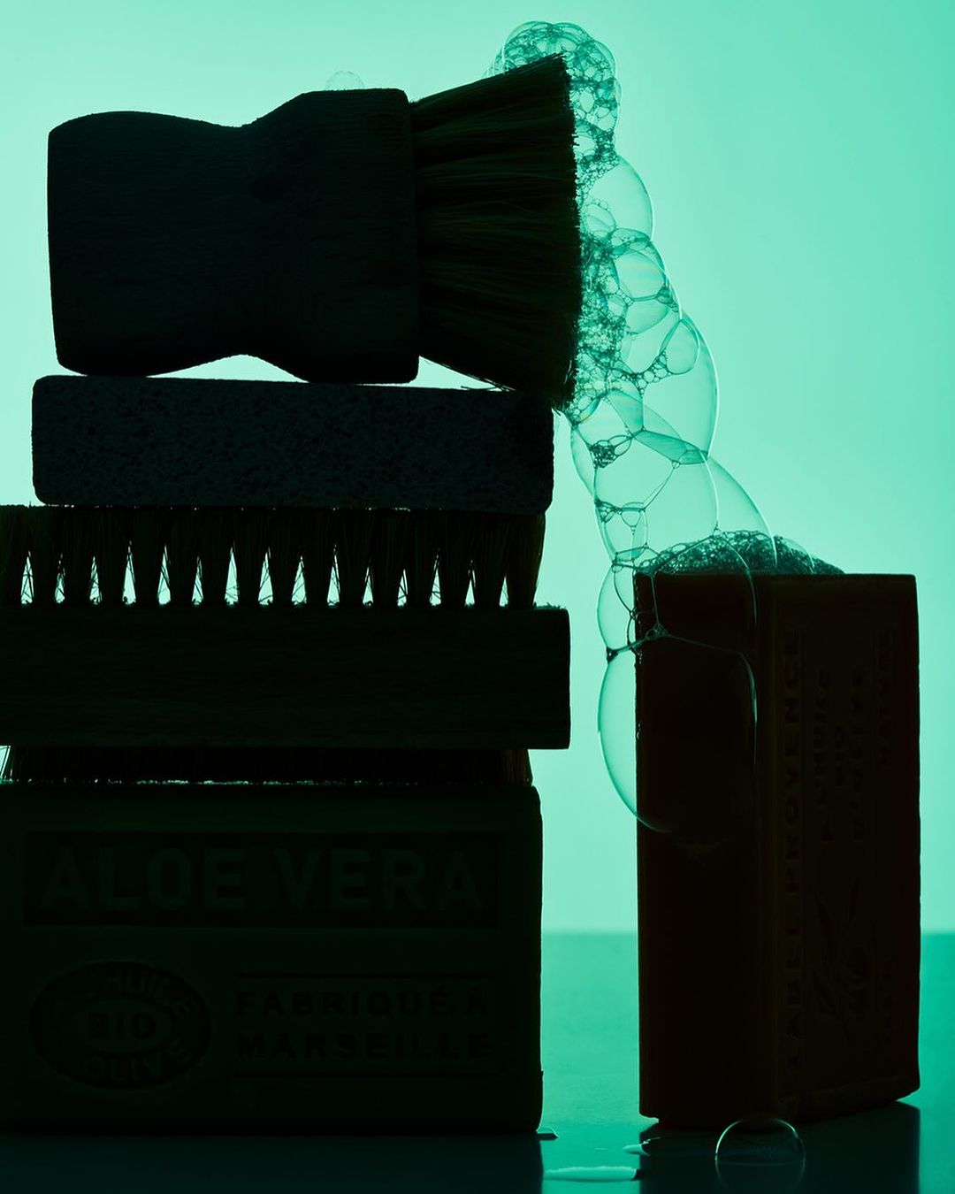 Stack of cleaning brushes and soap with bubbles, creating a still life composition against a vibrant green backdrop.