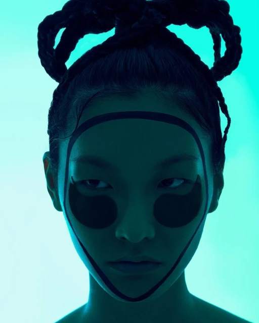 Close-up portrait of a stylish adult woman with hair in braided buns, wearing dark makeup design against a light blue background.