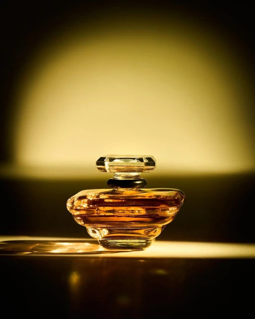 A close-up studio shot of a vintage-style transparent glass perfume bottle with amber liquid, illuminated by a spotlight against a gradient backdrop.