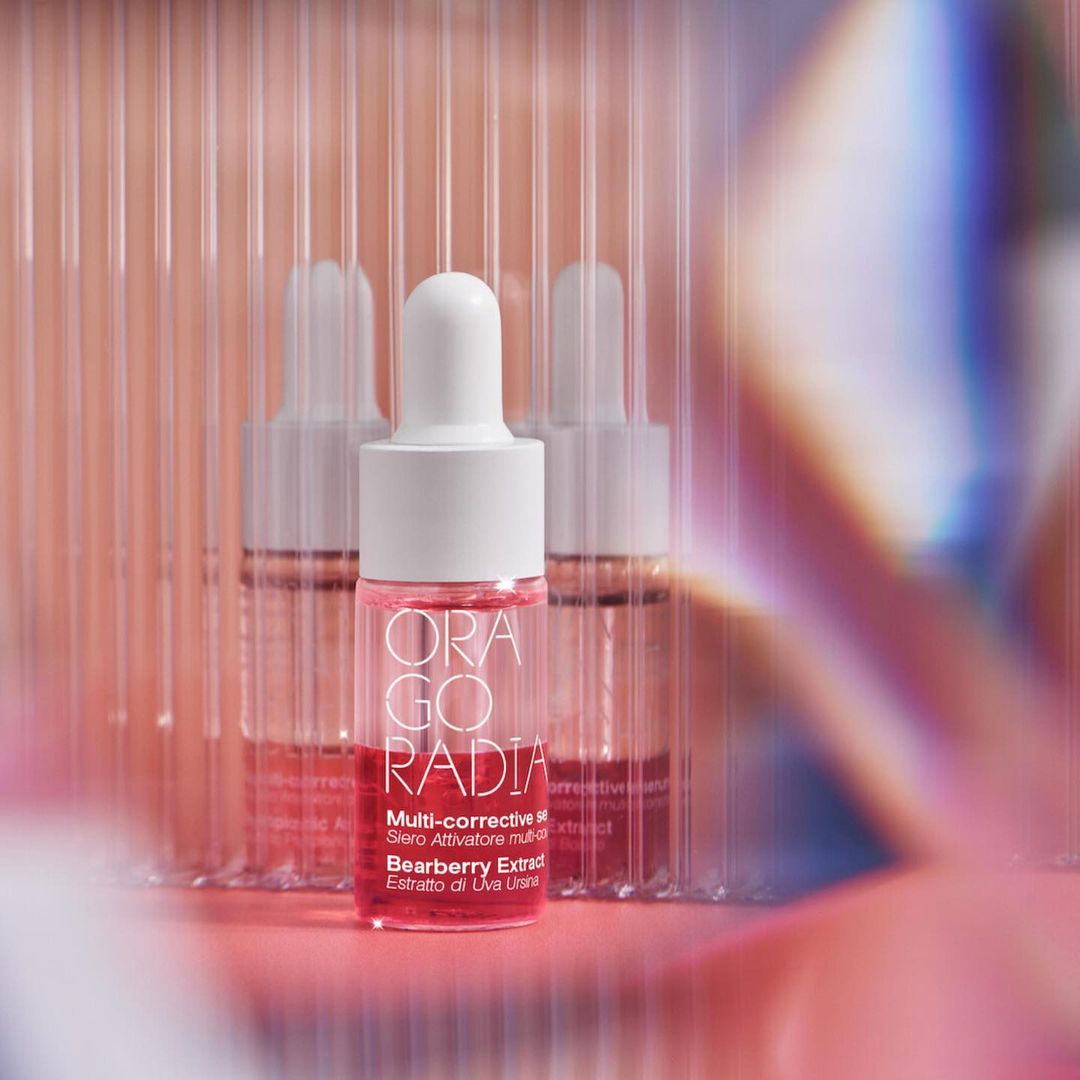 Close-up of Orago Radia serum bottles against a pink-toned background with light refraction effects, highlighting the skincare product's packaging.