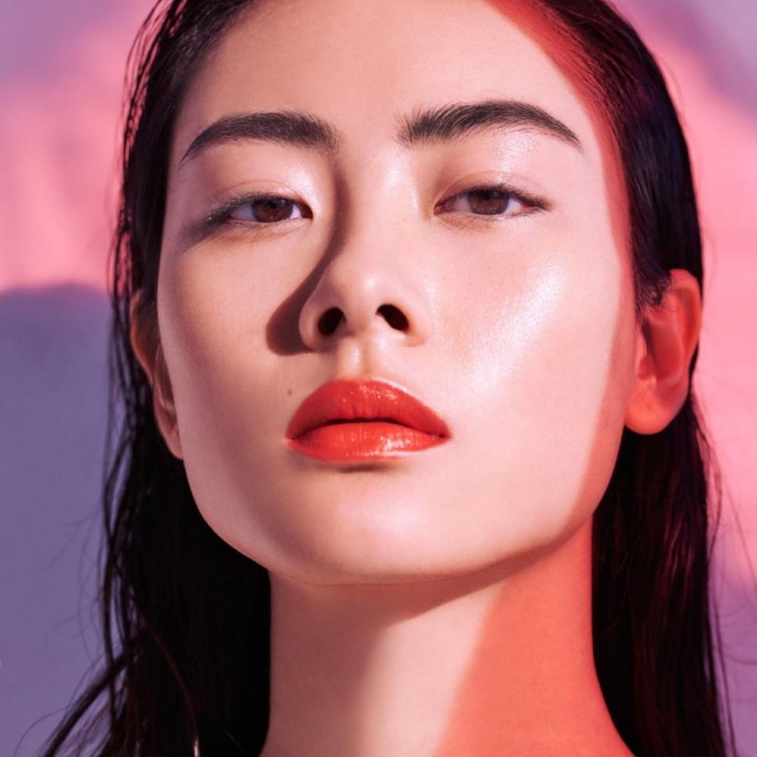 Close-up of a beautiful Asian woman with red lipstick, illuminated by soft pink and purple lighting, showcasing makeup and beauty.