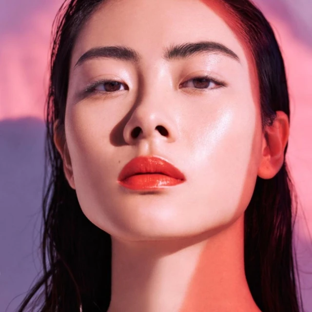 Close-up of a beautiful Asian woman with red lipstick, illuminated by soft pink and purple lighting, showcasing makeup and beauty.