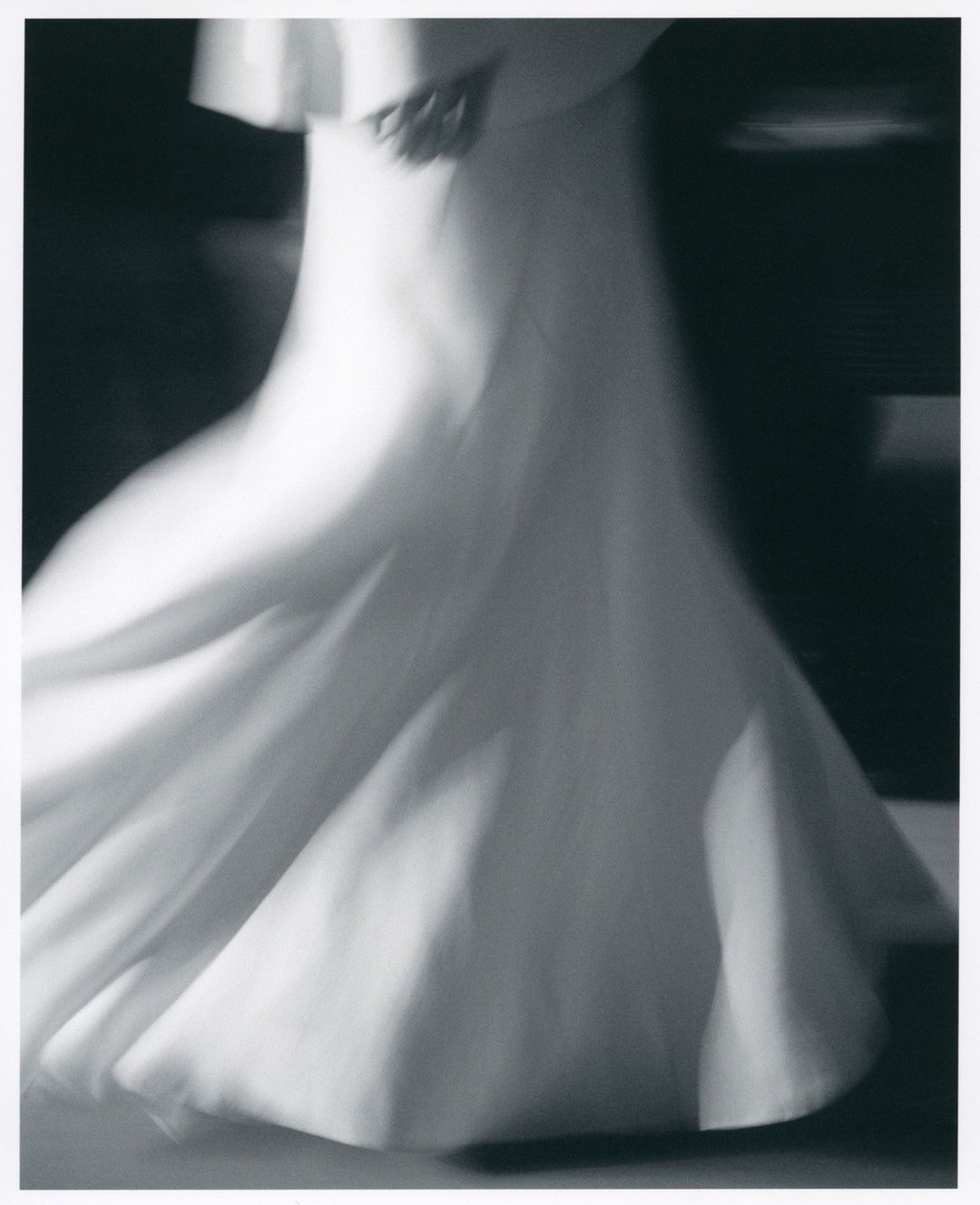 Abstract fashion photo featuring an adult female model in a white dress, captured with blurred motion and black and white tones.