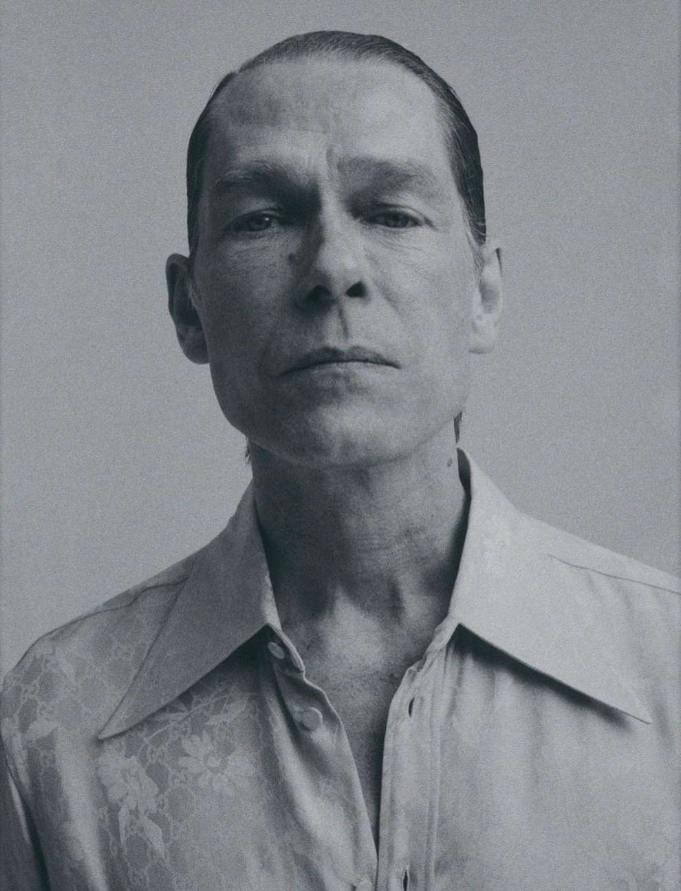 Monochrome portrait of a middle-aged man wearing a patterned shirt. Close-up shot focusing on his face with neutral expression.
