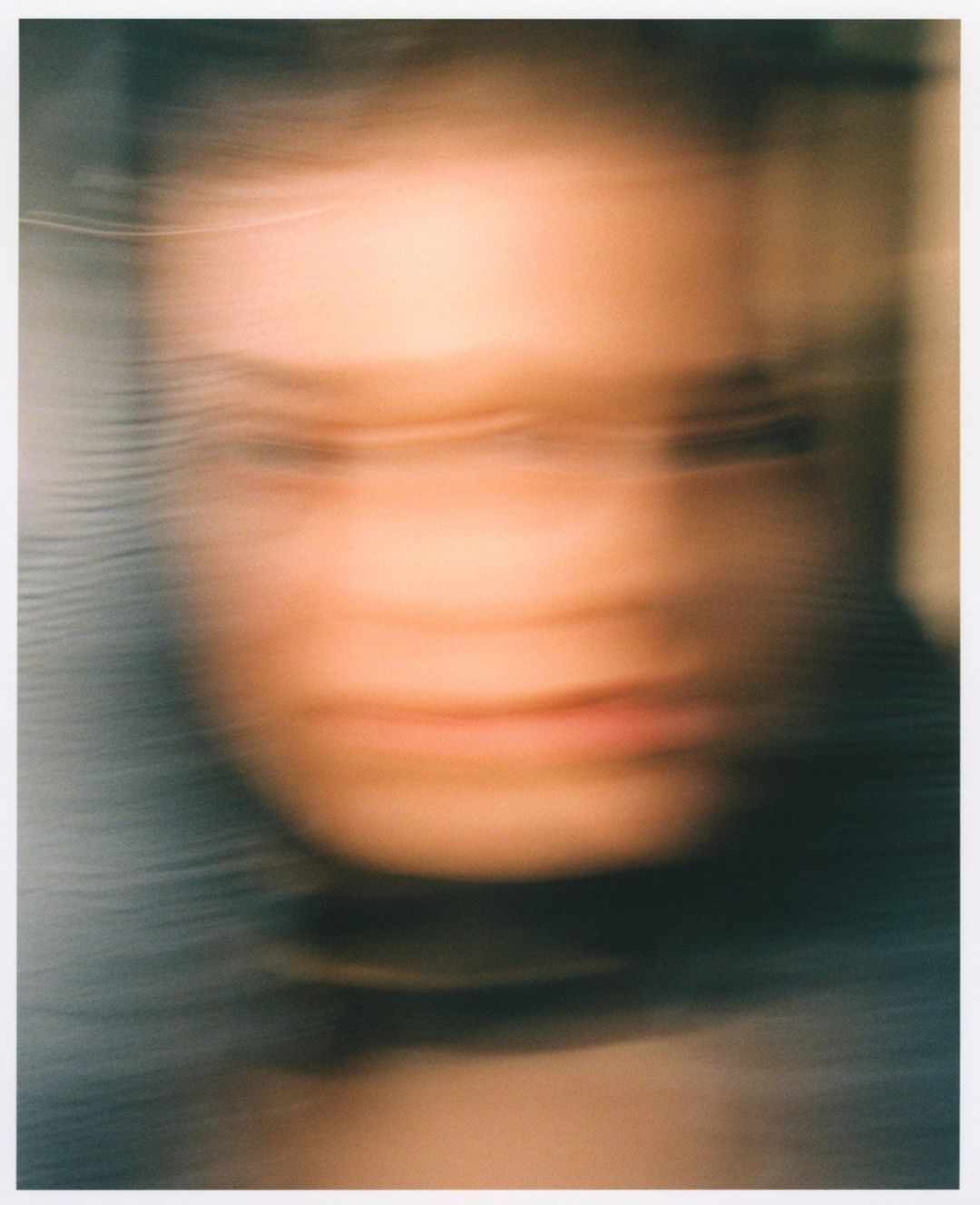 Blurred portrait of an adult female with fair skin, dark hair, wearing a dark top, indistinct background, soft lighting, and artistic blur.