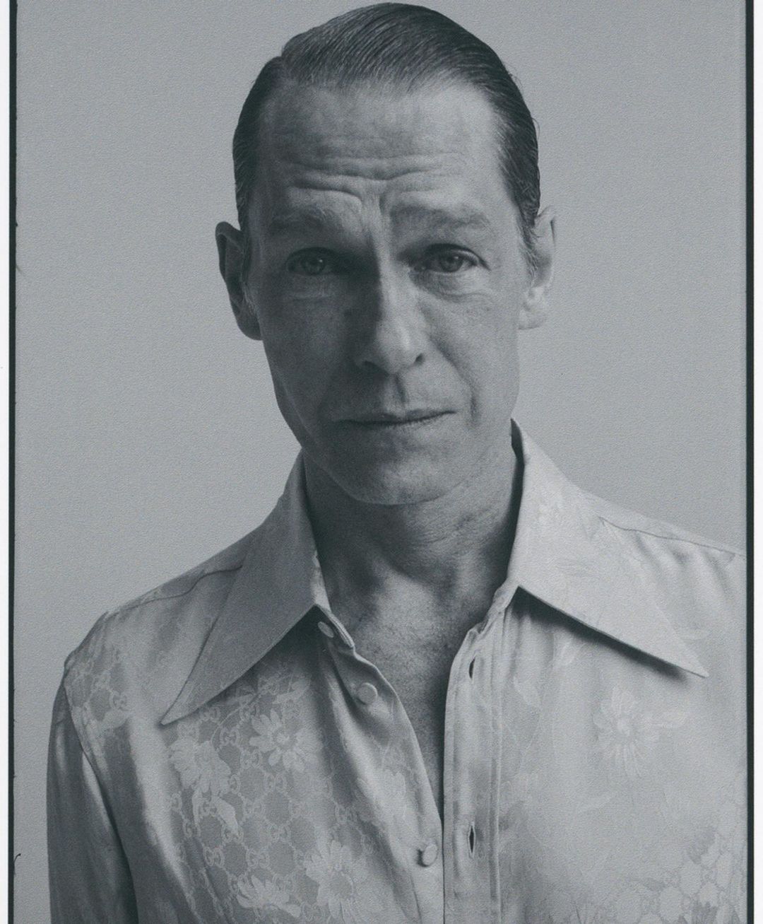 Monochromatic portrait of an adult male with light skin, wearing a patterned shirt. The subject is against a neutral background.