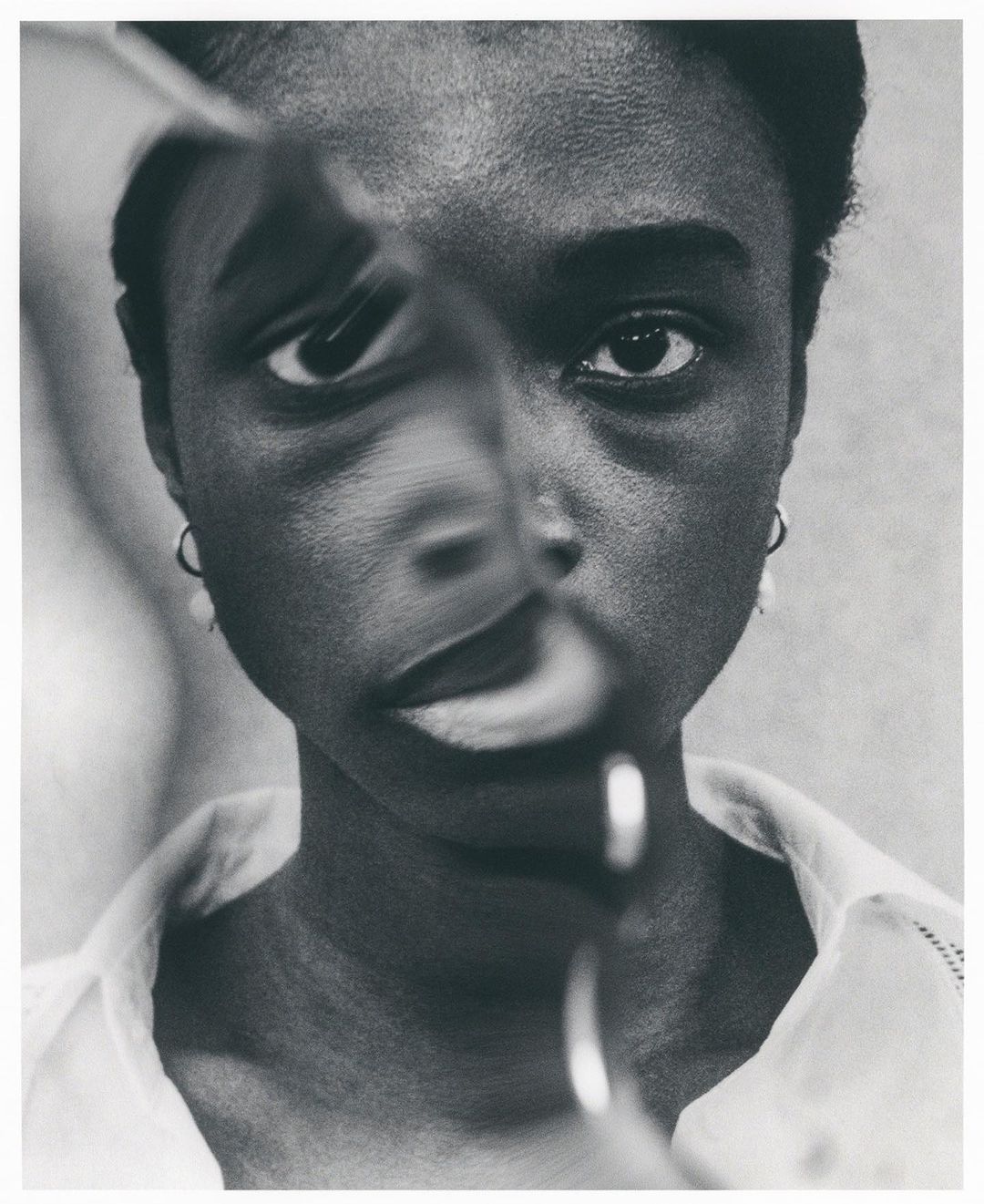 Monochrome portrait of a woman, distorted by a magnifying glass, indoors, with fair lighting and neutral background. The focus is on her face.