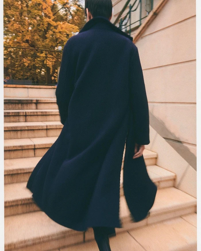 Rear view of a person wearing a long navy blue coat walking up stone outdoor stairs in Frankfurt.