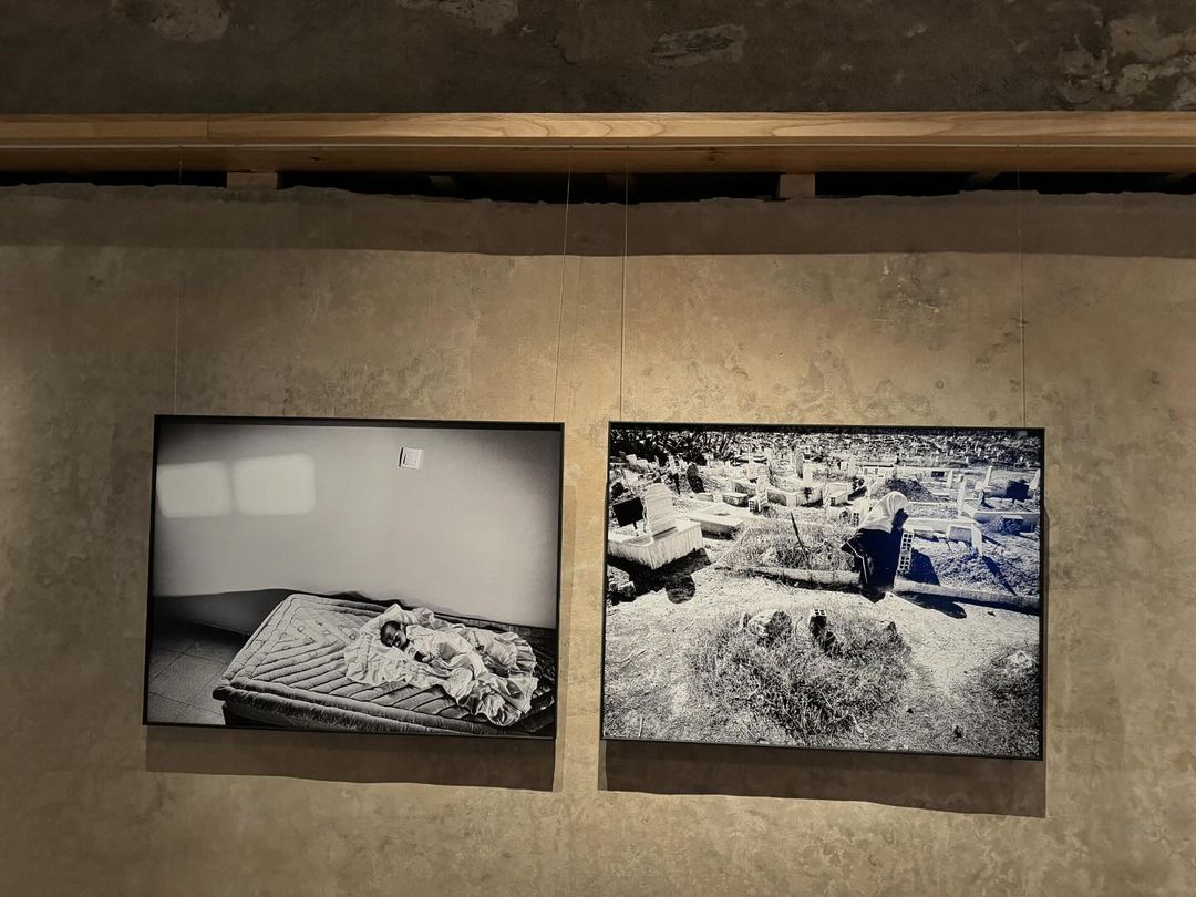 Black and white photograph of a person on a mattress next to a photograph of a city in a room setting with exposed beam.