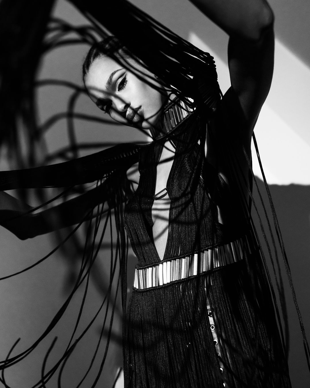 Black and white portrait of an adult female model in dark fringe dress with heavy eye makeup and shadow play on a neutral background.