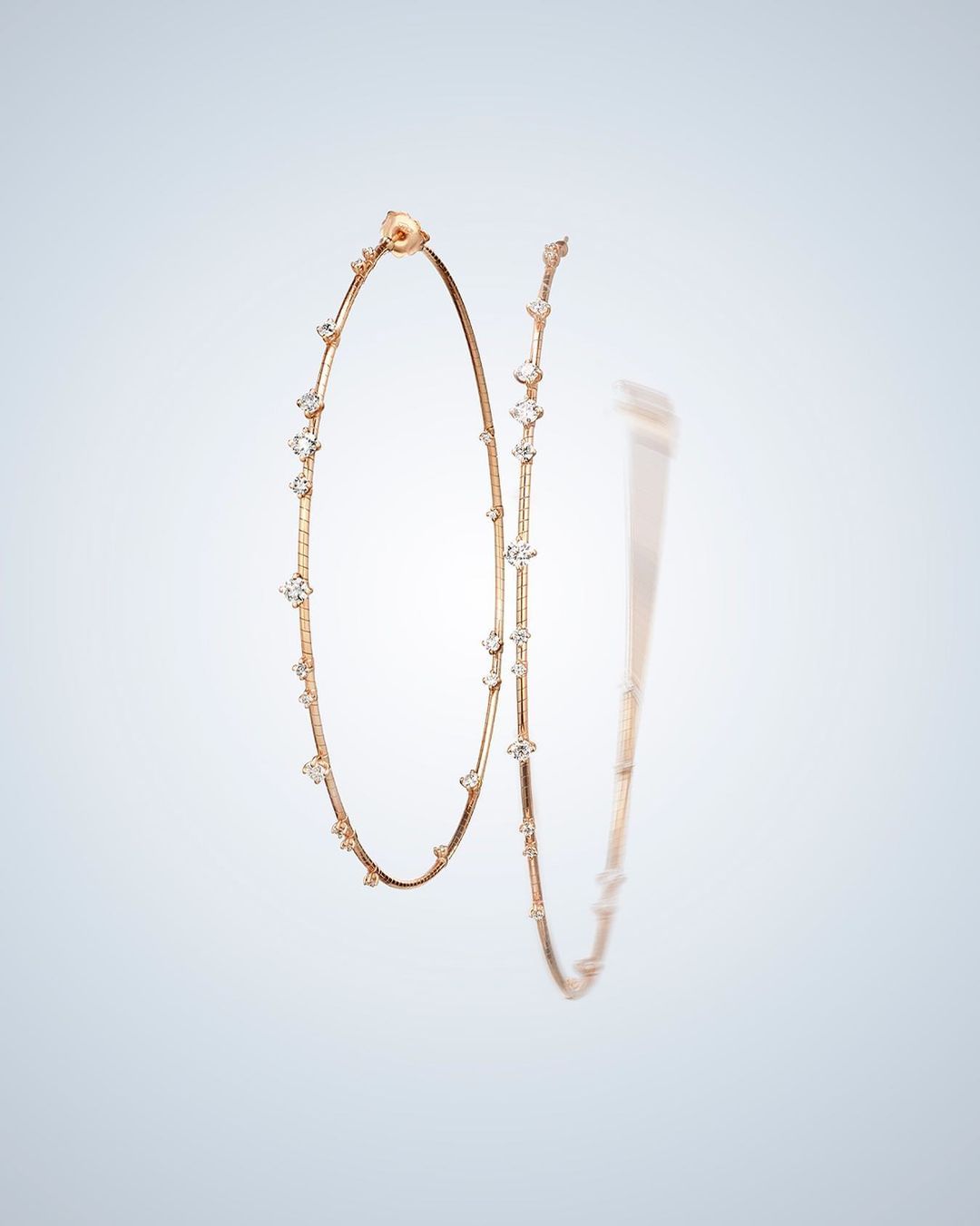 Elegant hoop earrings in rose gold tone, adorned with clear gemstones, are showcased against a soft gradient background.