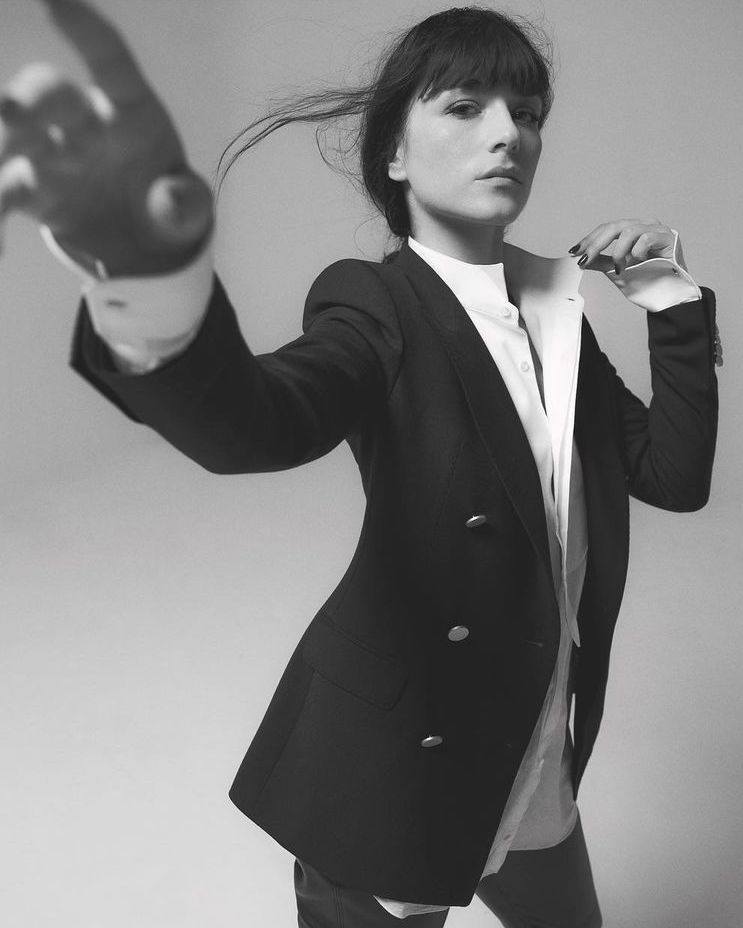 Monochrome portrait of an adult woman in a black blazer over a white shirt, posing against a plain backdrop in a studio setting.