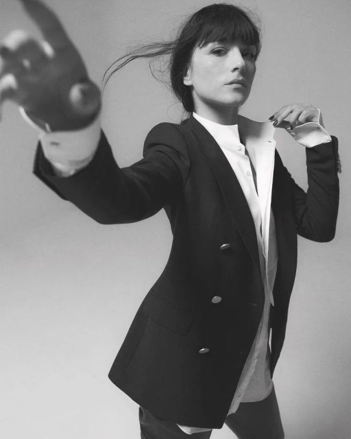 Monochrome portrait of an adult woman in a black blazer over a white shirt, posing against a plain backdrop in a studio setting.