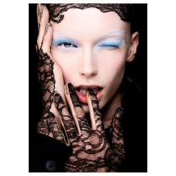 Close-up portrait of a woman wearing black lace gloves and headpiece with light blue eye makeup, photographed by Filippo Fortis.