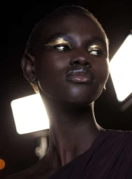 Close-up portrait of a black woman with metallic gold eye makeup and dark clothing photographed by Filippo Fortis in Milan.