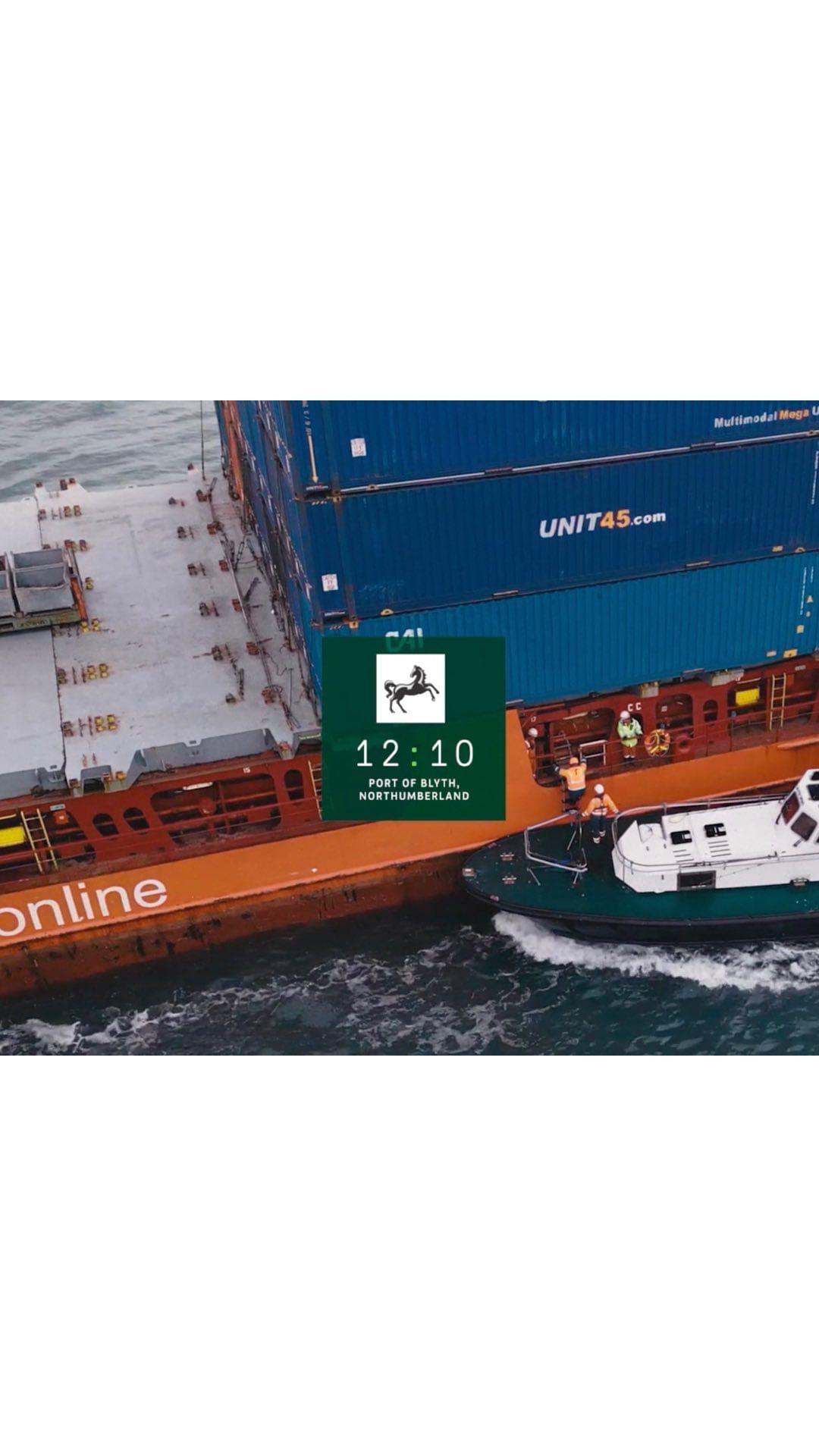 Aerial view of a cargo ship being assisted by a tugboat in the sea, carrying stacked containers on its deck.  Shipping industry.