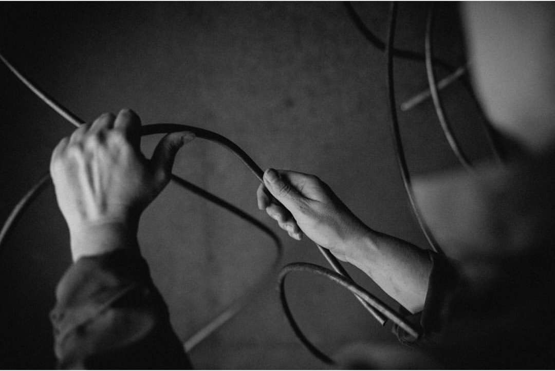 Black and white studio shot of hands holding a black wire, set against a dark, textured background with additional wires. 