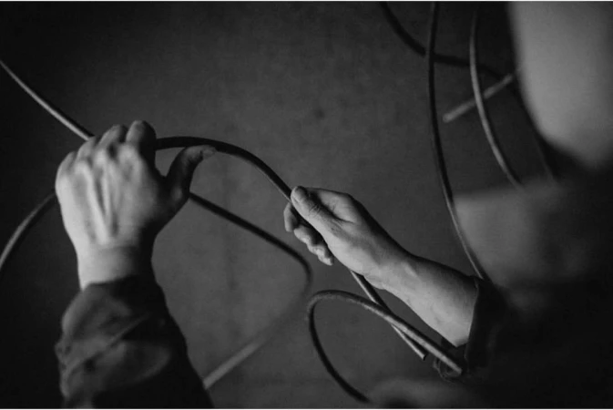 Black and white studio shot of hands holding a black wire, set against a dark, textured background with additional wires. 