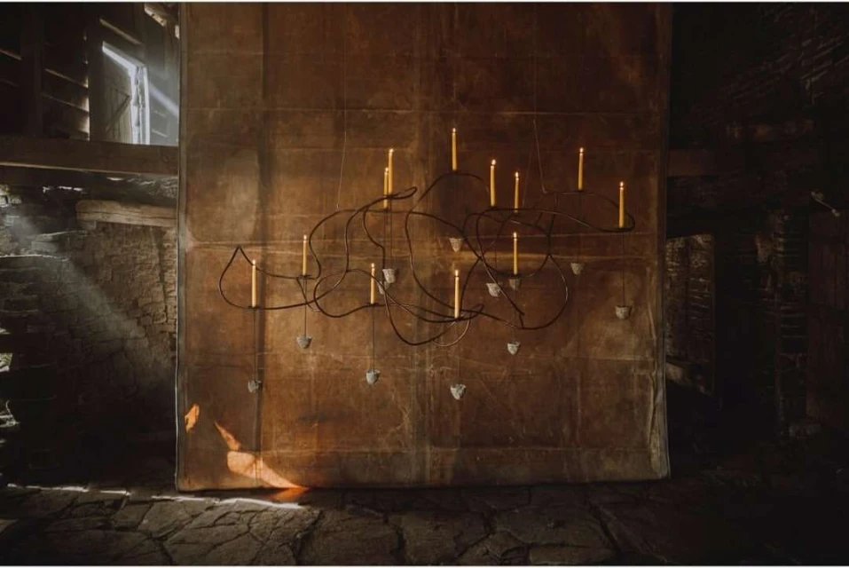 Interior view of an illuminated chandelier featuring lit candles, suspended from a dark, textured ceiling in a rustic space.