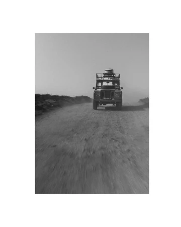 Black and white shot of Land Rover SUV driving on a dirt road with barren land and a dusty sky. Automotive, adventure, off-road.