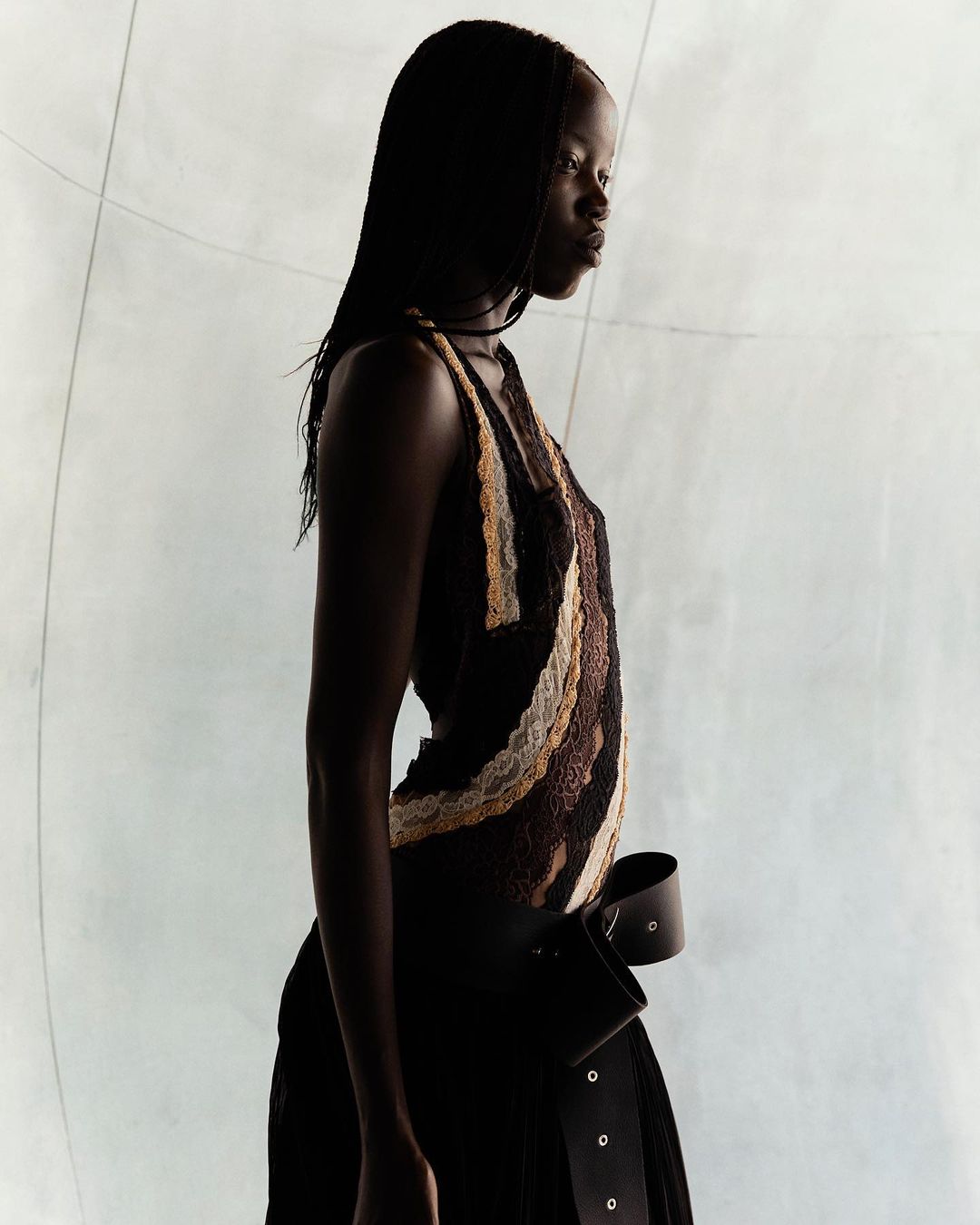 Studio shot of a Black woman in a textured brown and tan dress with a wide leather belt, against a muted, soft-lit neutral background.