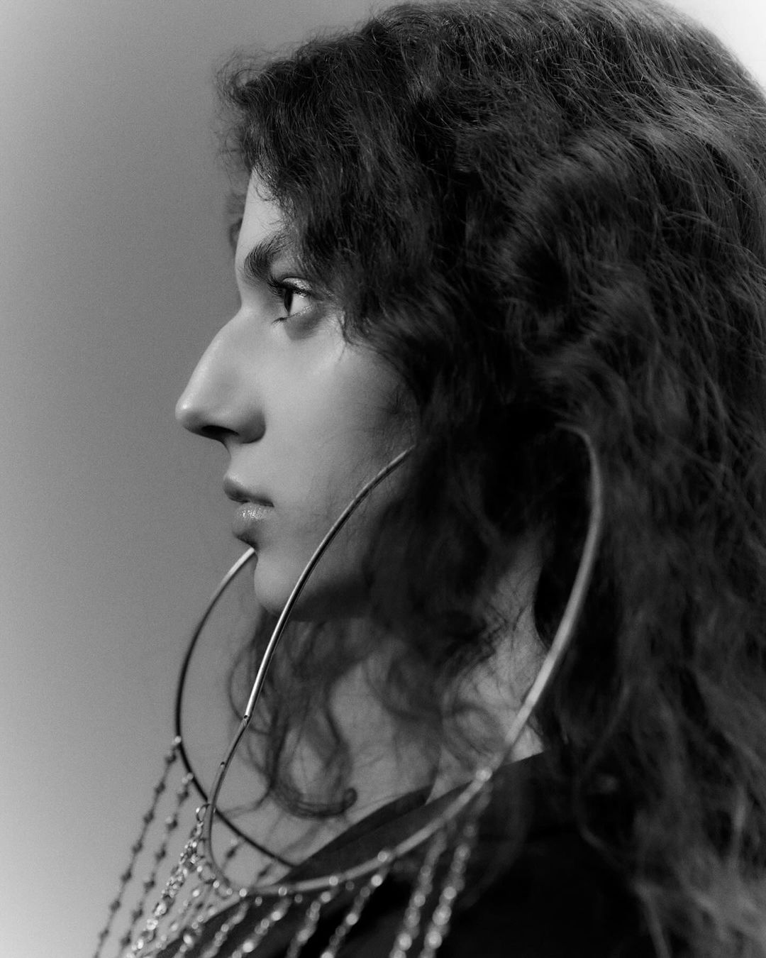 Profile portrait of a woman with long curly hair wearing large dangling hoop earrings in monochrome.