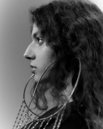 Profile portrait of a woman with long curly hair wearing large dangling hoop earrings in monochrome.