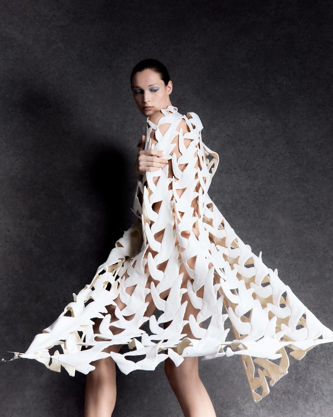 Elegant woman poses in white sculptural dress against grey backdrop. Fashion photography with stylish clothing and studio lighting, striking visual.