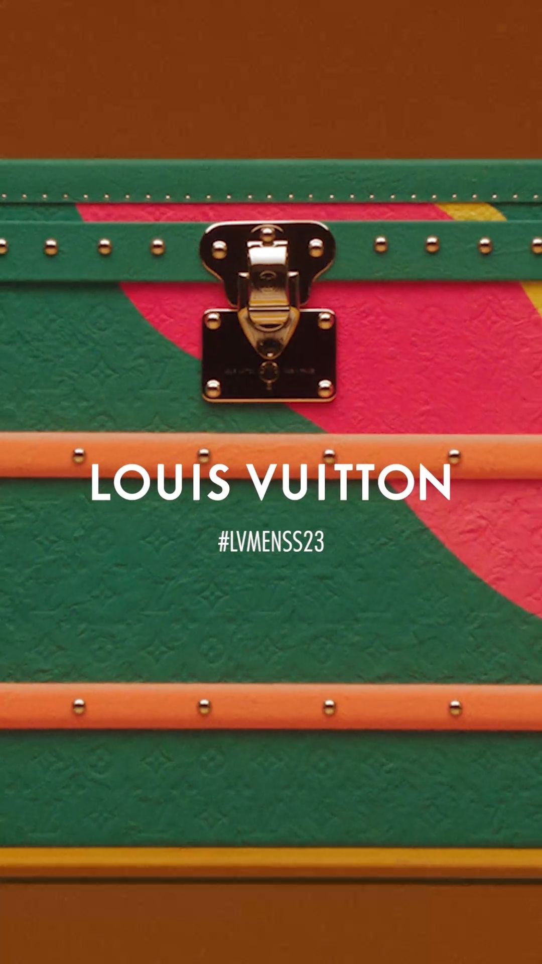 Detailed shot of a Louis Vuitton trunk with a unique orange, green, and pink painted design and gold hardware details.
