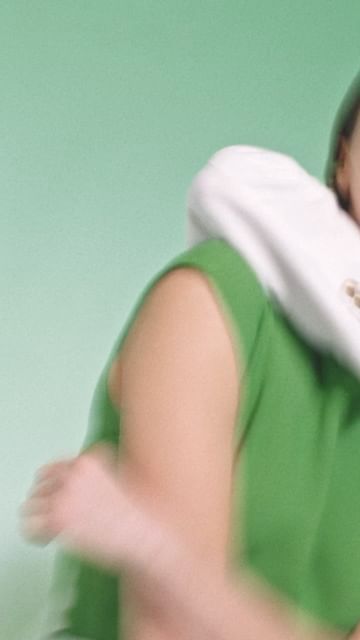 Blurred action shot of a person in a green shirt and a white hooded sweatshirt, facing away, against a solid light green background.