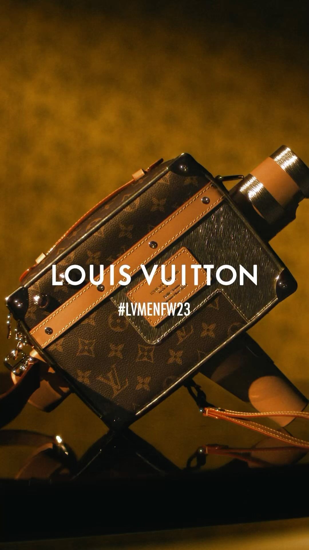 Louis Vuitton brown monogrammed box camera bag with brown leather trim and a tan background, photographed in a close-up shot.