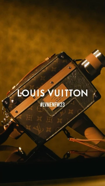 Louis Vuitton brown monogrammed box camera bag with brown leather trim and a tan background, photographed in a close-up shot.