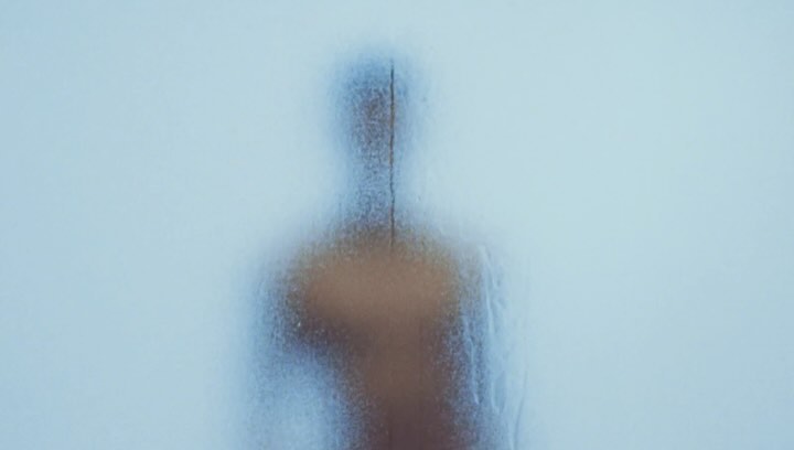 Abstract image featuring a blurred figure behind frosted glass, emphasizing texture and light in an enigmatic and minimalist composition.
