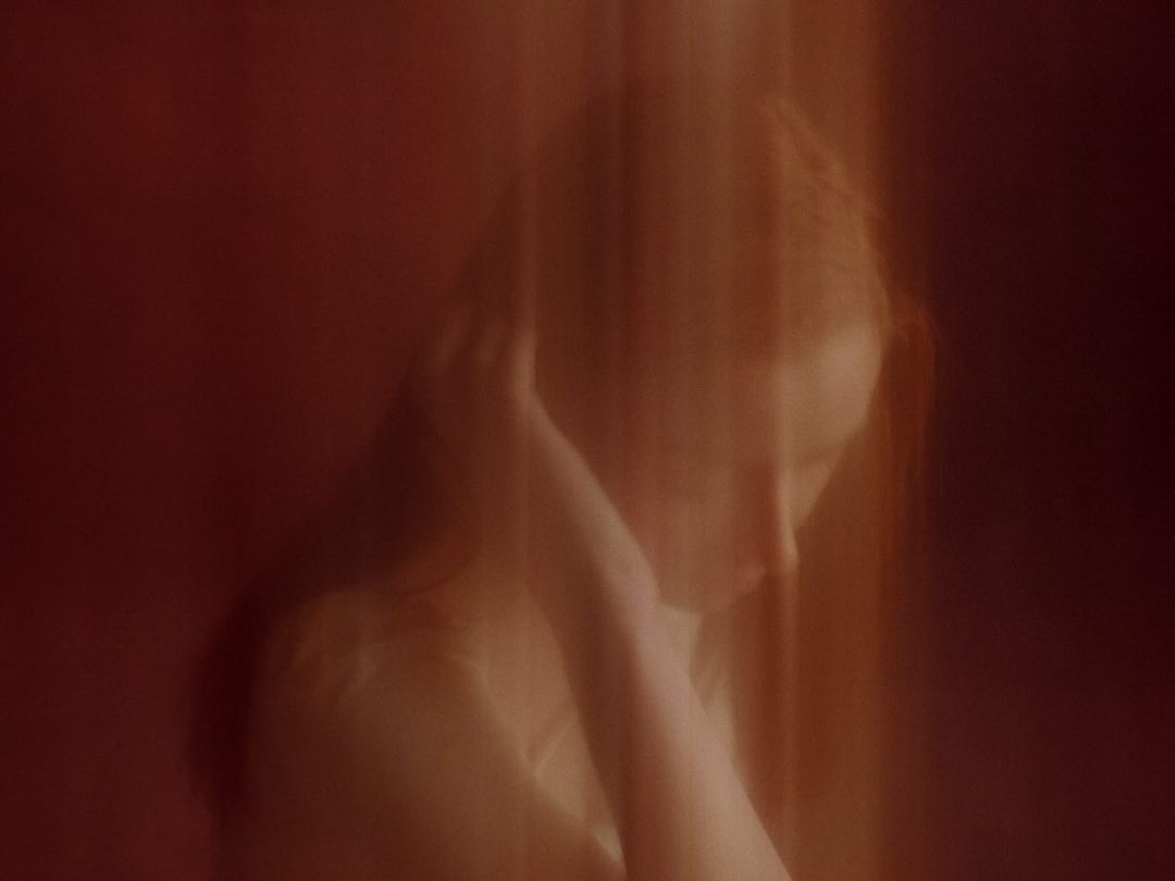 Portrait of an adult female with long red hair, posing indoors with dramatic lighting and blurred motion, in a beauty or fashion context.