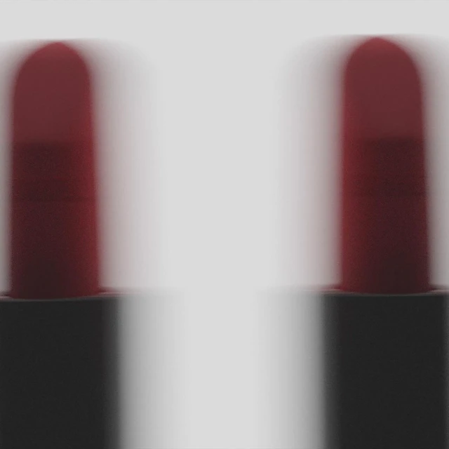 Close-up shot of two red lipsticks with blurred motion effect against a pale grey background in studio lighting for a beauty theme.