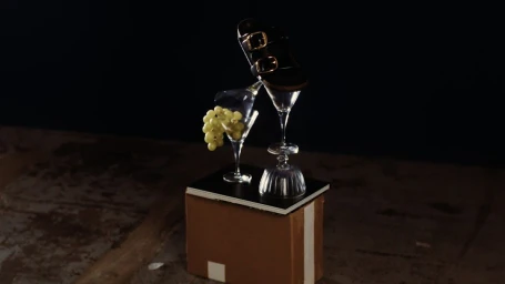 Black leather double-buckle sandal balanced on stacked glassware with green grapes, photographed by Florent Augizeau.