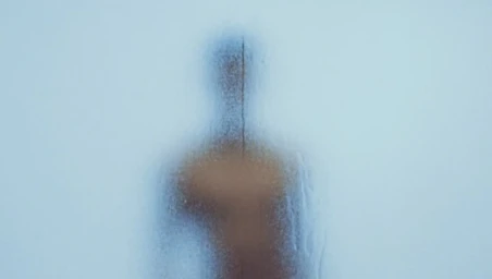 Silhouette of a person visible through a frosted glass panel with visible moisture droplets and a vertical streak.
