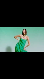 Woman with dark short hair wearing a vibrant green slip dress against a pale turquoise seamless background.