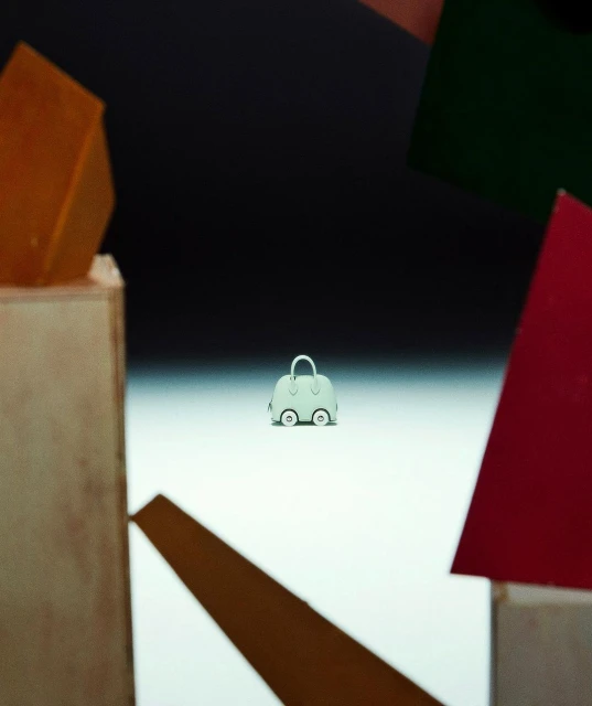 Light blue handbag with small wheels on a white surface, surrounded by various geometric blocks and set against a dark backdrop.