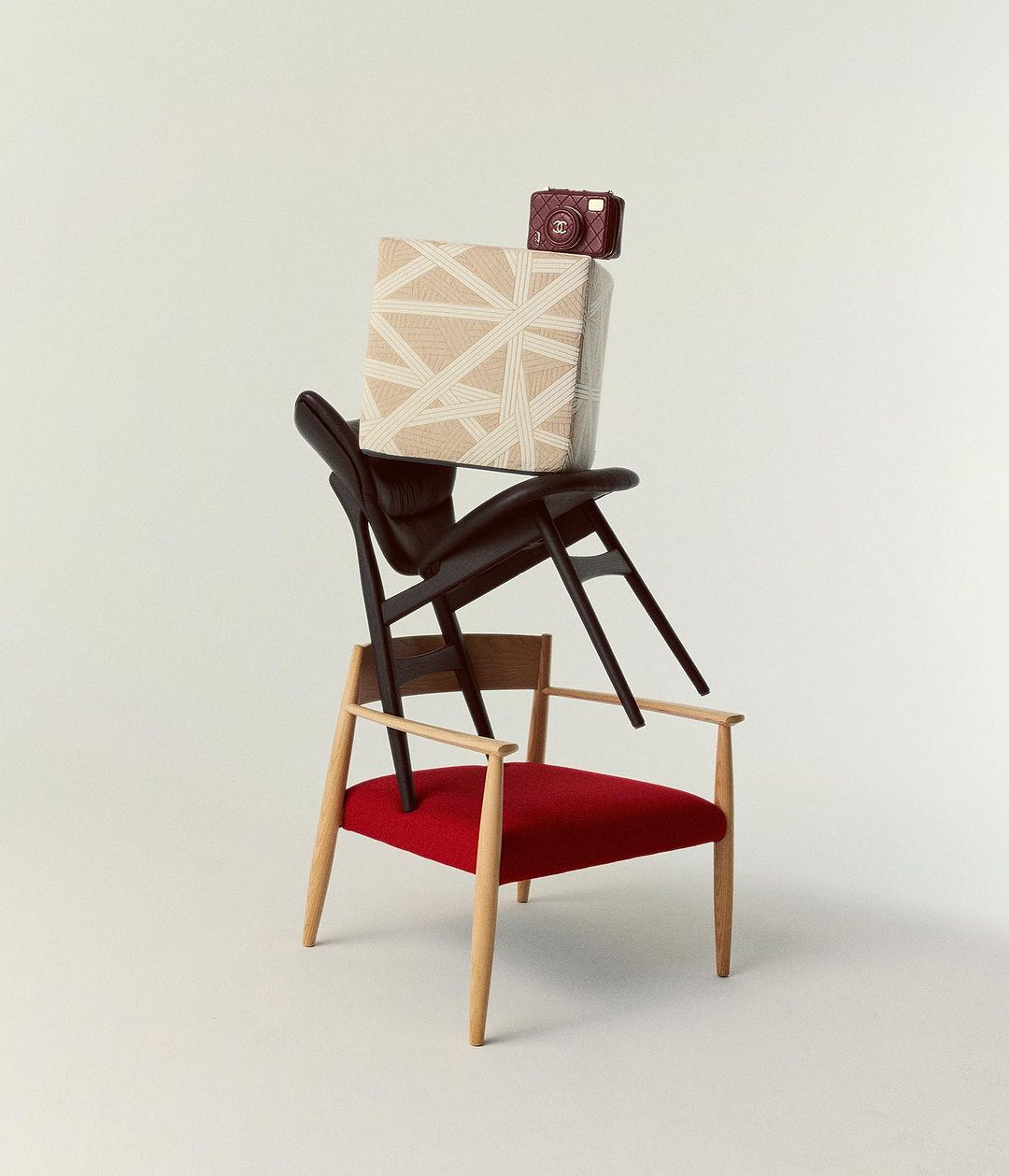 Stack of designer chairs and a decorative cube topped with a small camera in a minimalist studio with a bright, solid off-white background.
