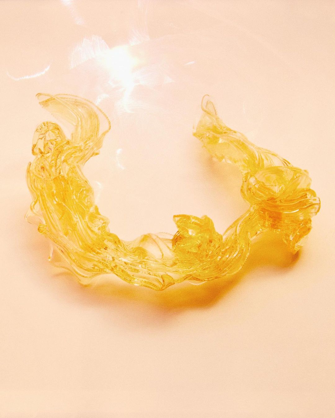 Translucent amber ribbon-like object on a peach background with diffused lighting.